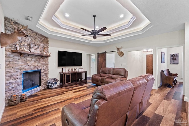living room with a tray ceiling, visible vents, a ceiling fan, wood finished floors, and a fireplace