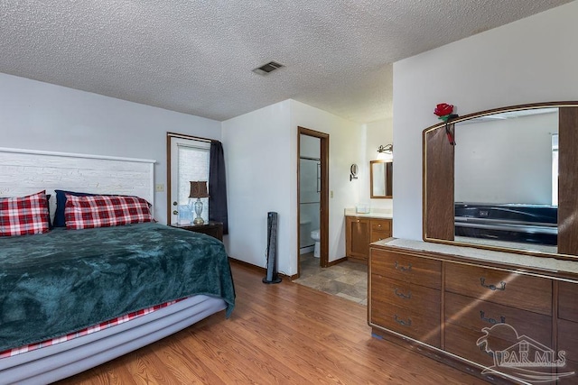 bedroom with light wood-style flooring, visible vents, a textured ceiling, and ensuite bathroom