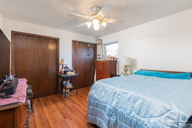 bedroom with light wood finished floors, ceiling fan, a textured ceiling, and multiple closets