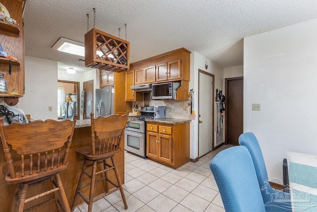 kitchen featuring open shelves, light countertops, appliances with stainless steel finishes, brown cabinetry, and under cabinet range hood