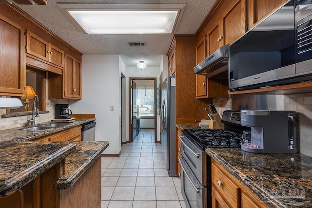 kitchen featuring a textured ceiling, under cabinet range hood, stainless steel appliances, a sink, and brown cabinets