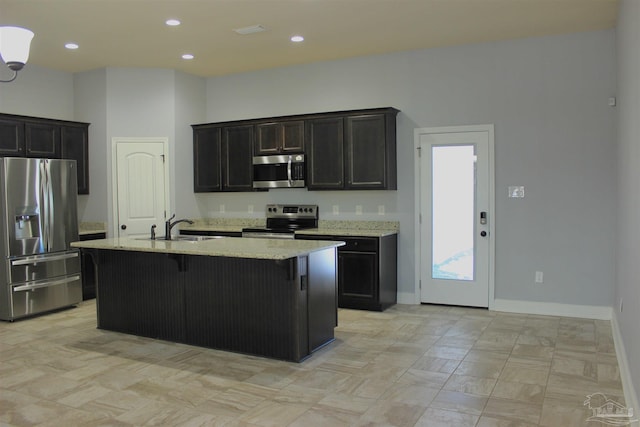 kitchen with sink, a breakfast bar area, a kitchen island with sink, stainless steel appliances, and light stone countertops