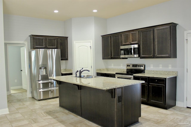 kitchen with sink, appliances with stainless steel finishes, dark brown cabinetry, light stone countertops, and an island with sink