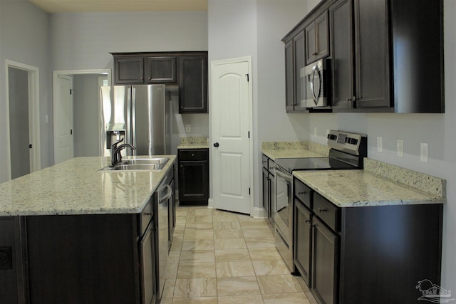 kitchen with stainless steel appliances, sink, a center island with sink, and light stone counters