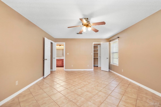 unfurnished bedroom with ceiling fan, a textured ceiling, a walk in closet, a closet, and light tile patterned floors