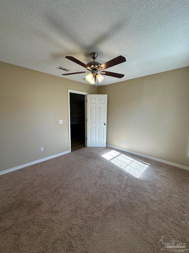 unfurnished bedroom with a walk in closet, a textured ceiling, carpet floors, and ceiling fan