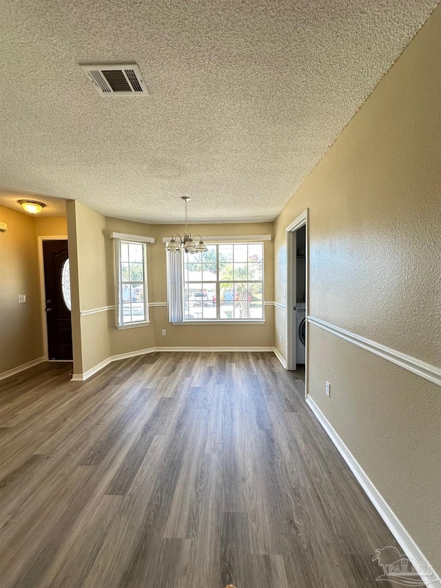 empty room with dark hardwood / wood-style flooring, a textured ceiling, washer / clothes dryer, and a chandelier