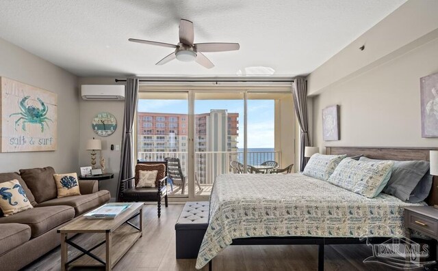 bedroom featuring hardwood / wood-style flooring, a wall mounted AC, a textured ceiling, access to exterior, and ceiling fan