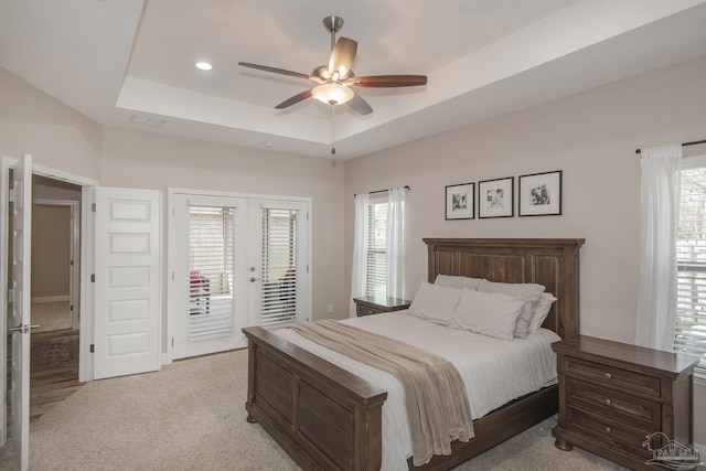 bedroom featuring access to exterior, french doors, a raised ceiling, and multiple windows