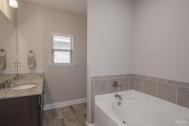 full bath with baseboards, wood finished floors, a bath, and vanity