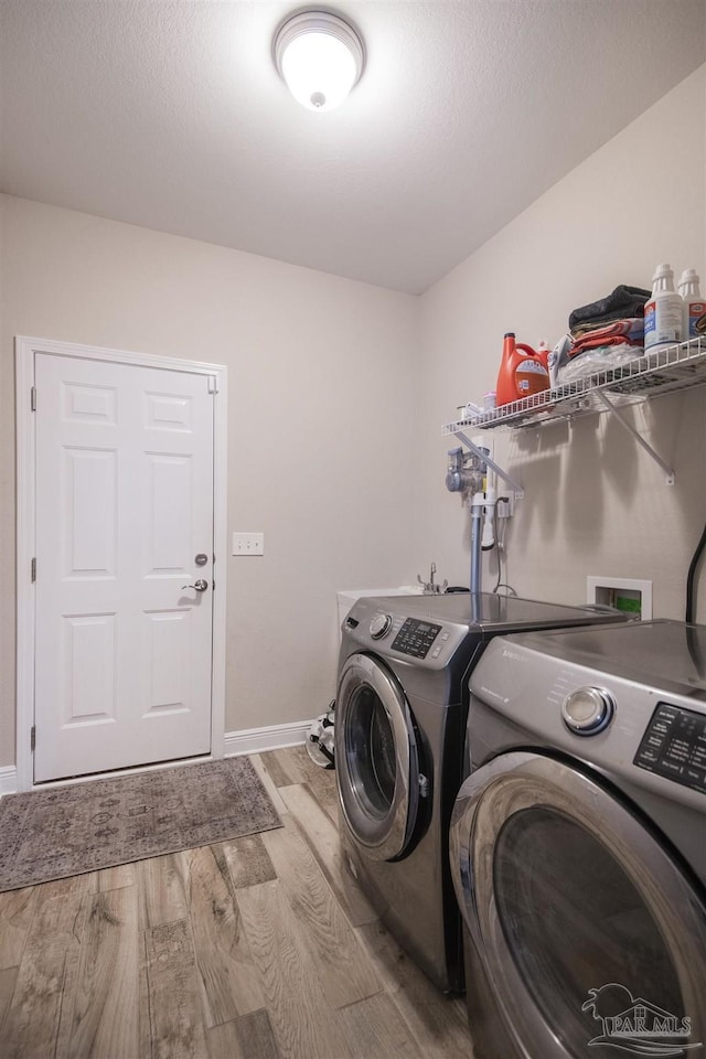 clothes washing area featuring a textured ceiling, laundry area, wood finished floors, baseboards, and washer and dryer