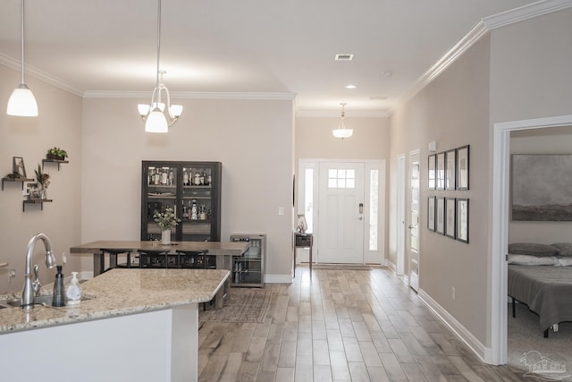 kitchen with light wood finished floors, ornamental molding, a sink, beverage cooler, and baseboards