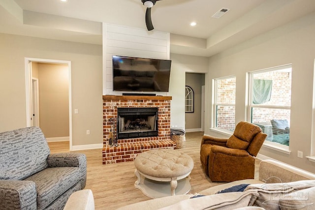 living room featuring a fireplace, light hardwood / wood-style floors, and a tray ceiling