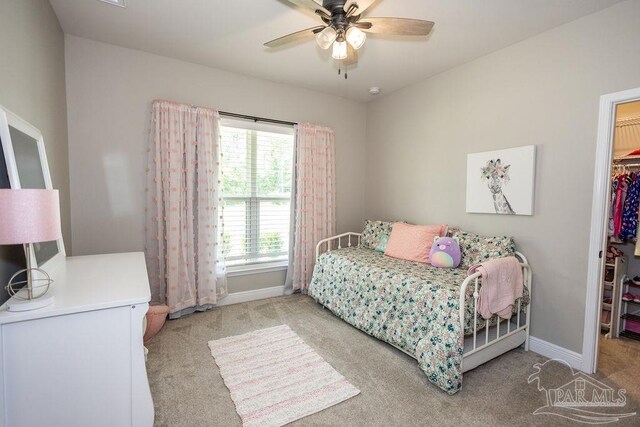 bedroom featuring a walk in closet, light colored carpet, a closet, and ceiling fan