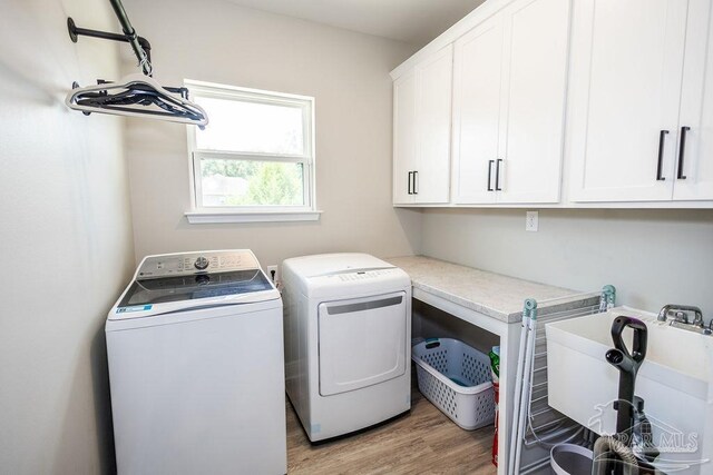 laundry area with washing machine and clothes dryer, light hardwood / wood-style floors, and cabinets