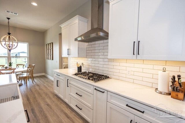 kitchen featuring white cabinetry, light wood-type flooring, wall chimney range hood, stainless steel gas cooktop, and decorative light fixtures