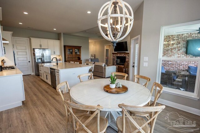 dining room featuring a fireplace, hardwood / wood-style flooring, and ceiling fan with notable chandelier