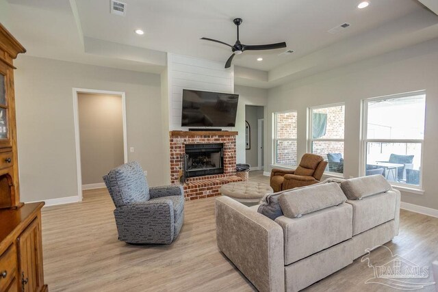 living room featuring ceiling fan, a brick fireplace, a raised ceiling, and light hardwood / wood-style floors