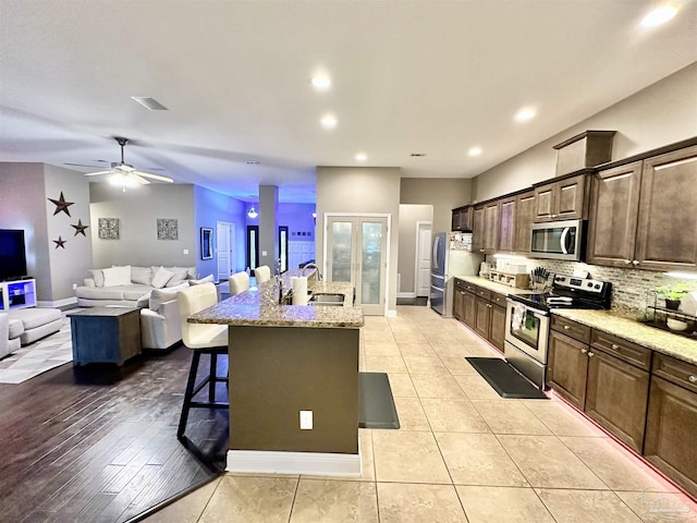 2924 Sundance Ln, Cantonment, FL 32533 - kitchen featuring appliances with stainless steel finishes, a kitchen bar, a center island with sink, backsplash, and light stone countertops