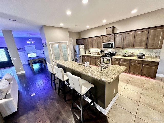 2924 Sundance Ln, Cantonment, FL 32533 - kitchen with stainless steel appliances, a kitchen breakfast bar, decorative backsplash, dark brown cabinetry, and a kitchen island with sink