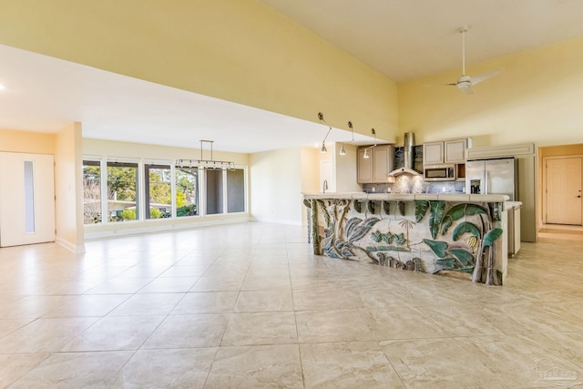 kitchen with ceiling fan, hanging light fixtures, wall chimney range hood, tasteful backsplash, and a kitchen breakfast bar