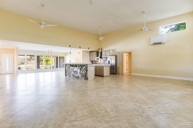 kitchen with a healthy amount of sunlight, a high ceiling, wall chimney range hood, and appliances with stainless steel finishes