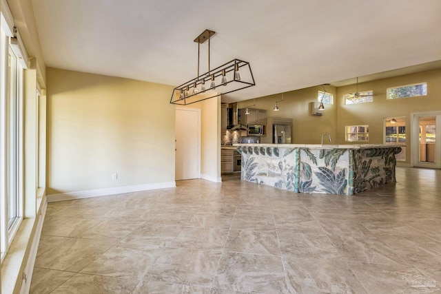 kitchen with decorative light fixtures, wall chimney range hood, and appliances with stainless steel finishes