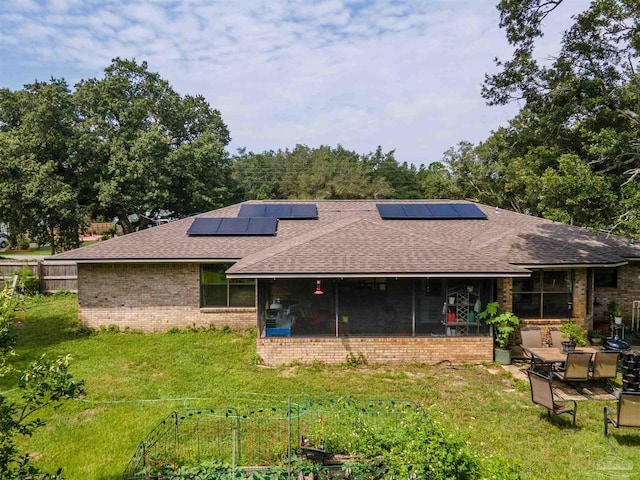 back of house featuring brick siding, roof with shingles, solar panels, a lawn, and a sunroom