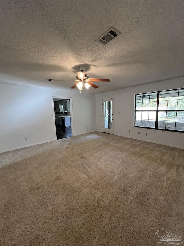 carpeted empty room featuring a textured ceiling, visible vents, and a ceiling fan