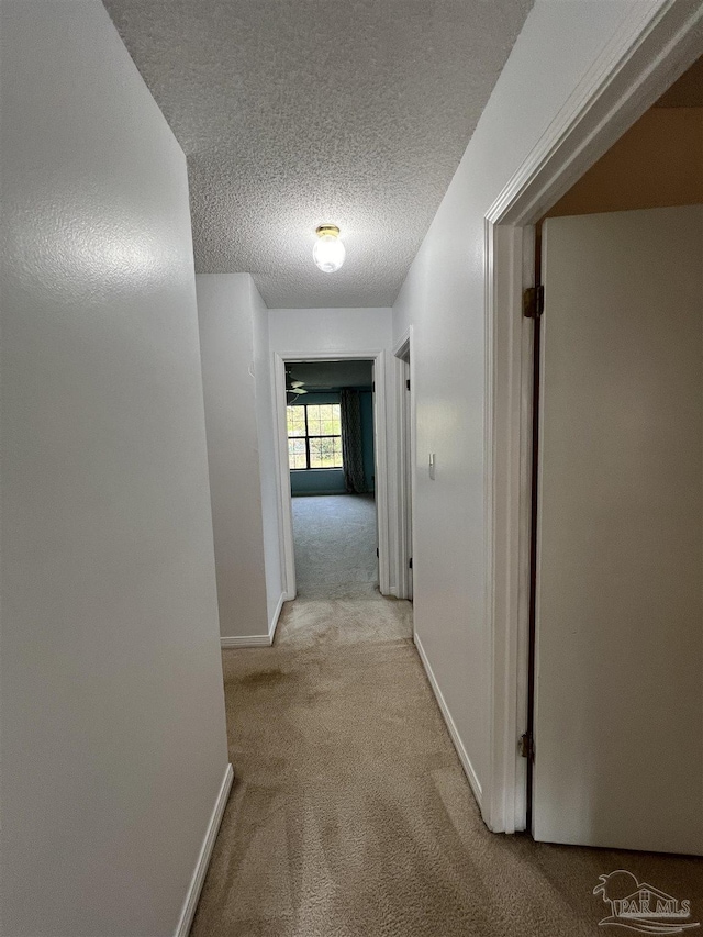 hallway featuring a textured ceiling, baseboards, and light colored carpet