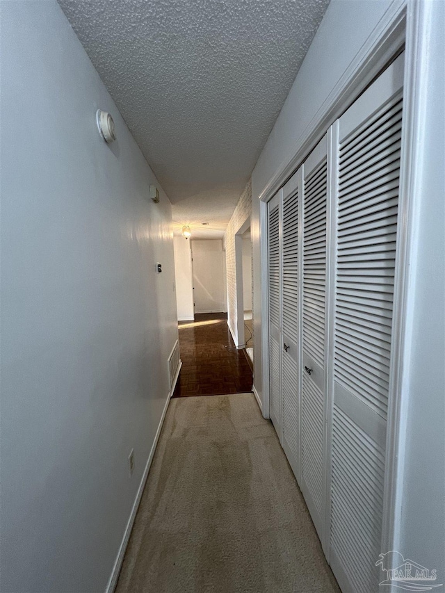 corridor featuring carpet, visible vents, a textured ceiling, and baseboards