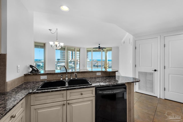 kitchen featuring dark stone countertops, dark tile patterned flooring, sink, black dishwasher, and ceiling fan with notable chandelier