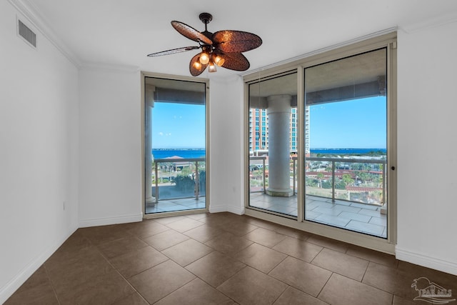 empty room with a wall of windows, dark tile patterned flooring, crown molding, ceiling fan, and a water view