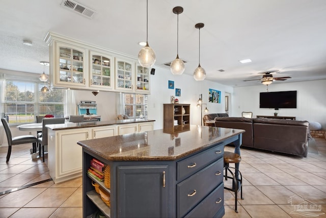 kitchen featuring light tile patterned floors, visible vents, ceiling fan, a center island, and a kitchen bar