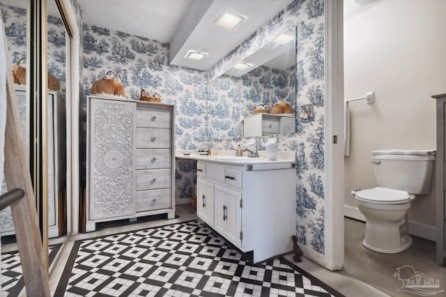 bathroom featuring baseboards, vanity, toilet, and wallpapered walls