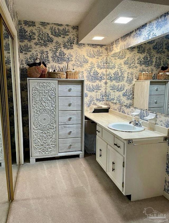 bathroom featuring a textured ceiling, vanity, and wallpapered walls