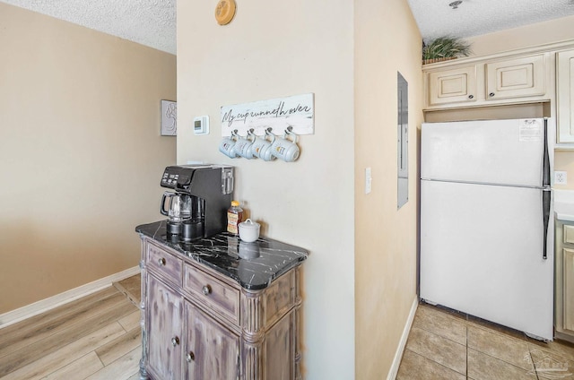 kitchen with cream cabinetry, freestanding refrigerator, a textured ceiling, dark stone counters, and baseboards