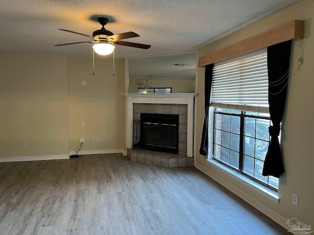 unfurnished living room with a tiled fireplace, ceiling fan, hardwood / wood-style floors, and a textured ceiling