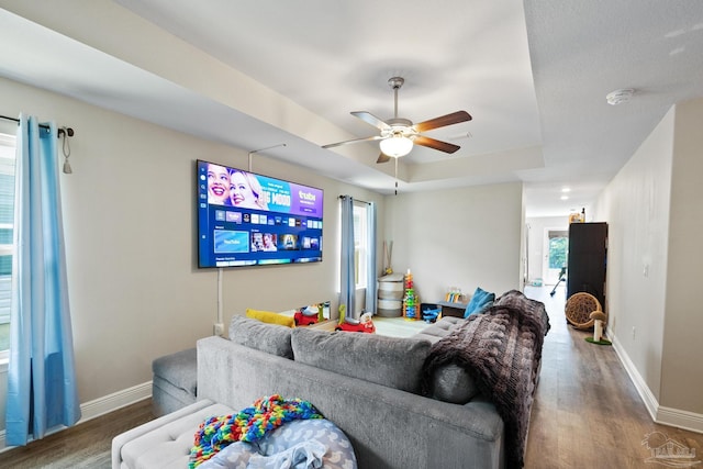 living area featuring ceiling fan, baseboards, a raised ceiling, and wood finished floors