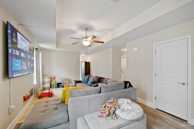 living room featuring baseboards, ceiling fan, a tray ceiling, and wood finished floors