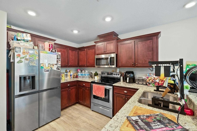 kitchen with light stone countertops, stainless steel appliances, light wood-style floors, and recessed lighting