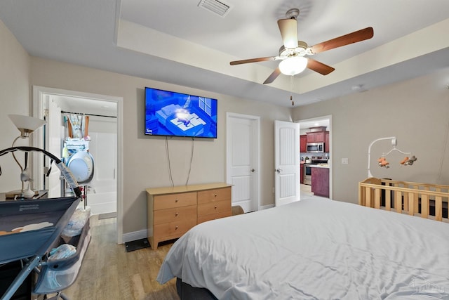 bedroom with a tray ceiling, visible vents, ceiling fan, light wood-type flooring, and baseboards