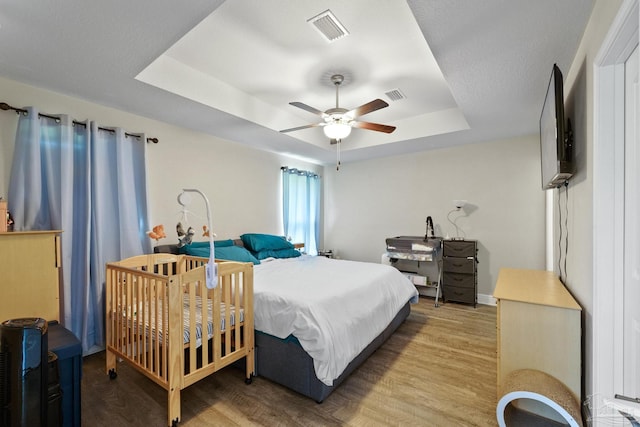 bedroom with light wood-type flooring, a raised ceiling, visible vents, and a ceiling fan