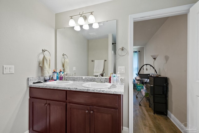 bathroom featuring wood finished floors, a sink, baseboards, and double vanity