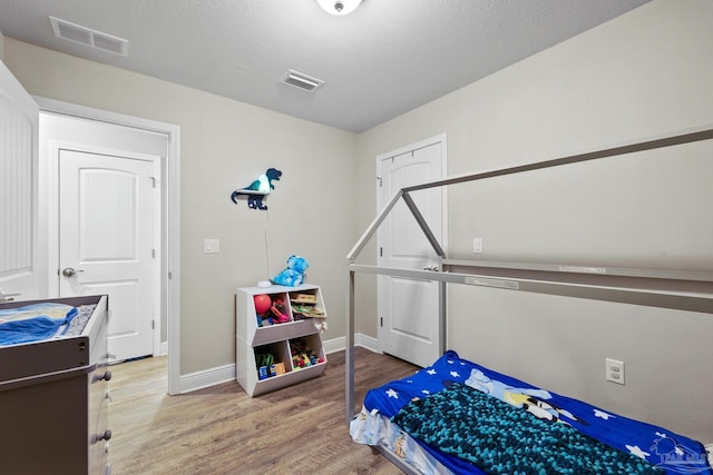 bedroom with baseboards, a textured ceiling, visible vents, and wood finished floors