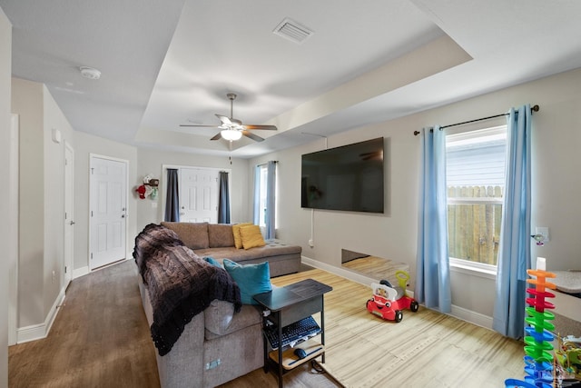 living room featuring baseboards, visible vents, a raised ceiling, and wood finished floors