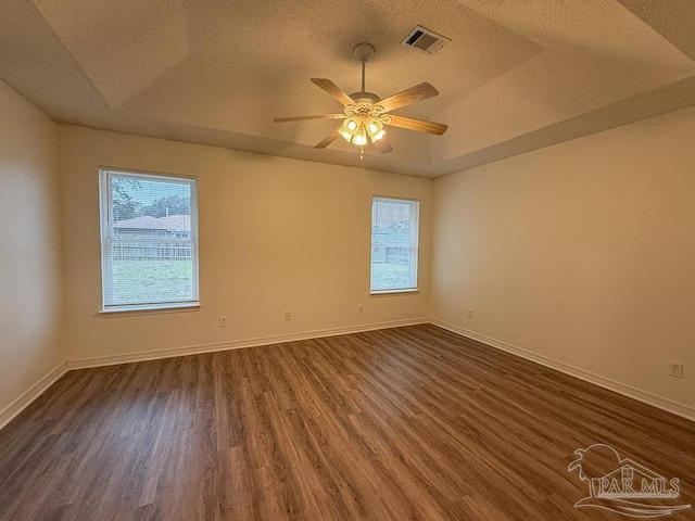 empty room featuring a textured ceiling, ceiling fan, dark wood-type flooring, and a tray ceiling