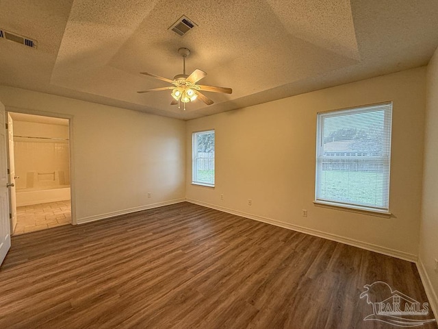 unfurnished room featuring dark hardwood / wood-style floors, ceiling fan, a textured ceiling, and a tray ceiling