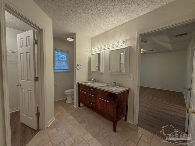 bathroom with a textured ceiling, vanity, toilet, and ceiling fan