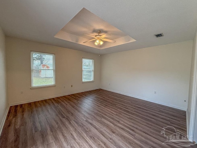 empty room with a raised ceiling, ceiling fan, dark hardwood / wood-style flooring, and a textured ceiling